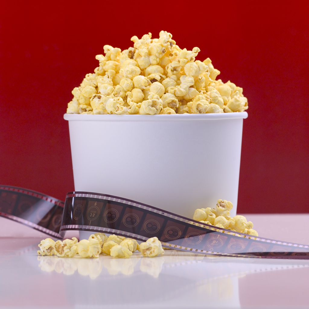 Container of popcorn on a table with a film reel.