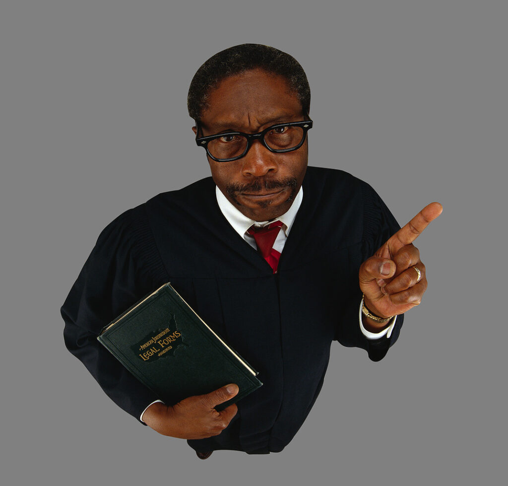 A judge is holding a law book in one hand and wagging his finger in the other.