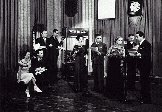 The popular program 'One Man's Family' is being broadcast from Studio 'C' at 111 Sutter Street, San Francisco, 1934. The program was heard on the NBC Pacific Coast Network. Shown are (left to right:) Kathleen Wilson (Claudia); Barton Yarbrough (Clifford); Bill Andrews (announcer); sound effects man Ed Ludes and his water effects machine; Bernice Berwin (Hazel); Mike Raffetto (Paul Barbour); Minetta Ellen (Mother Barbour); Page Gilman (Jack); J. Anthony Smythe (Father Barbour).