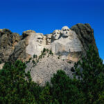 A close up of a large rock with Mount Rushmore National Memorial in the background.